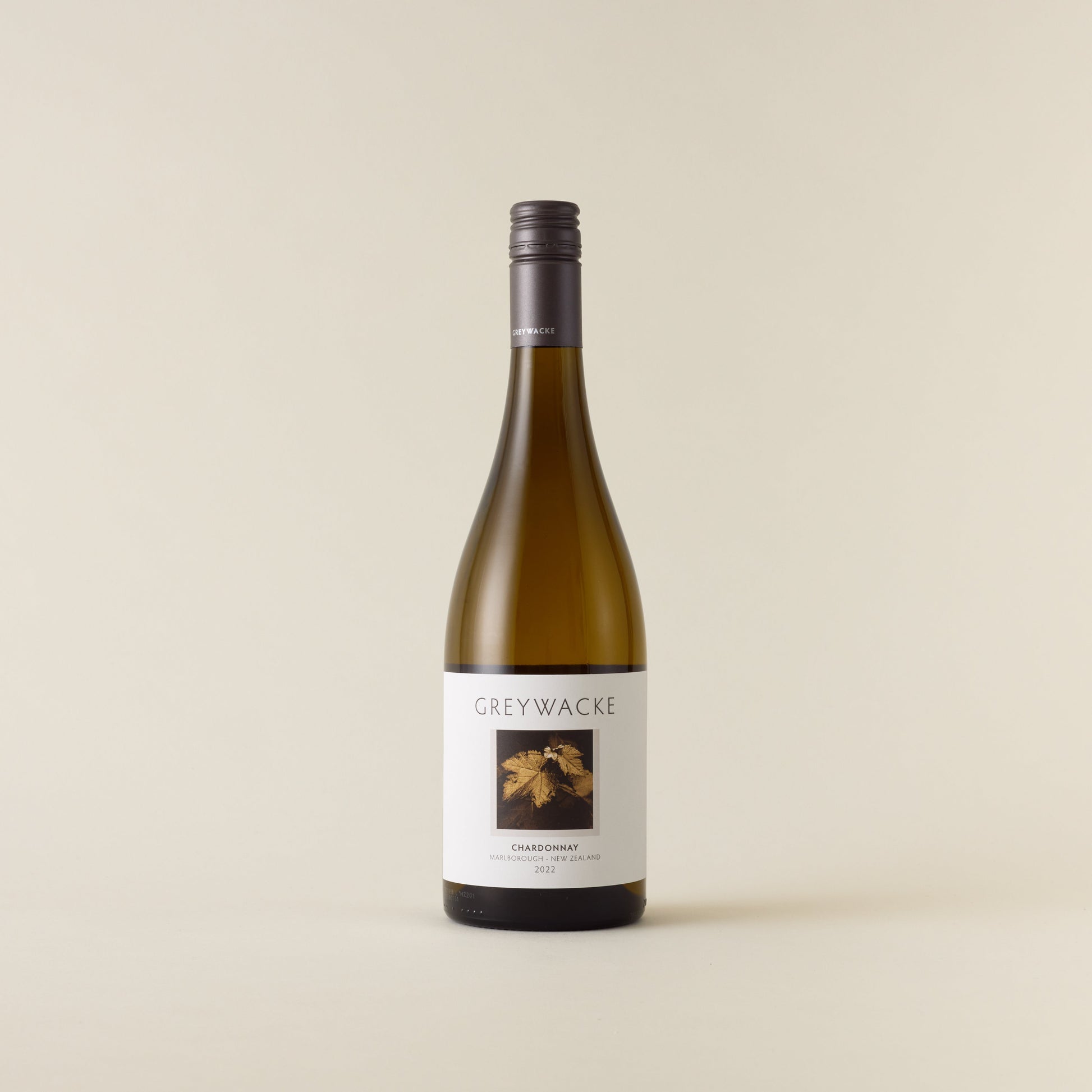 White wine bottle with chardonnay wine inside. A white label with Greywacke logo and image of vine leaf. A matte grey screwcap and neck label.